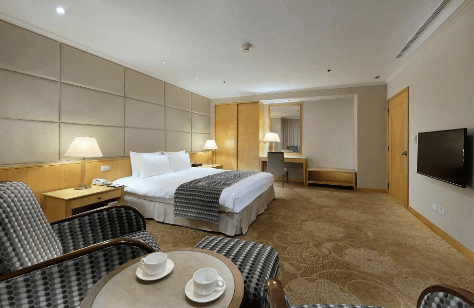 【中壢夜市住宿】中壢米堤大飯店豪華雙人房，房內配置一張大床與兩張沙發椅，並附設茶几、電視與辦公桌，營造舒適典雅的住宿氛圍。