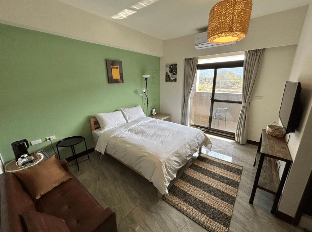 【竹山住宿】伍伍七 Local Supply 單人景觀房型，綠色牆面搭配自然採光，設有雙人床、沙發、陽台與山景視野，整體風格簡約清新，營造自在放鬆的住宿氛圍。