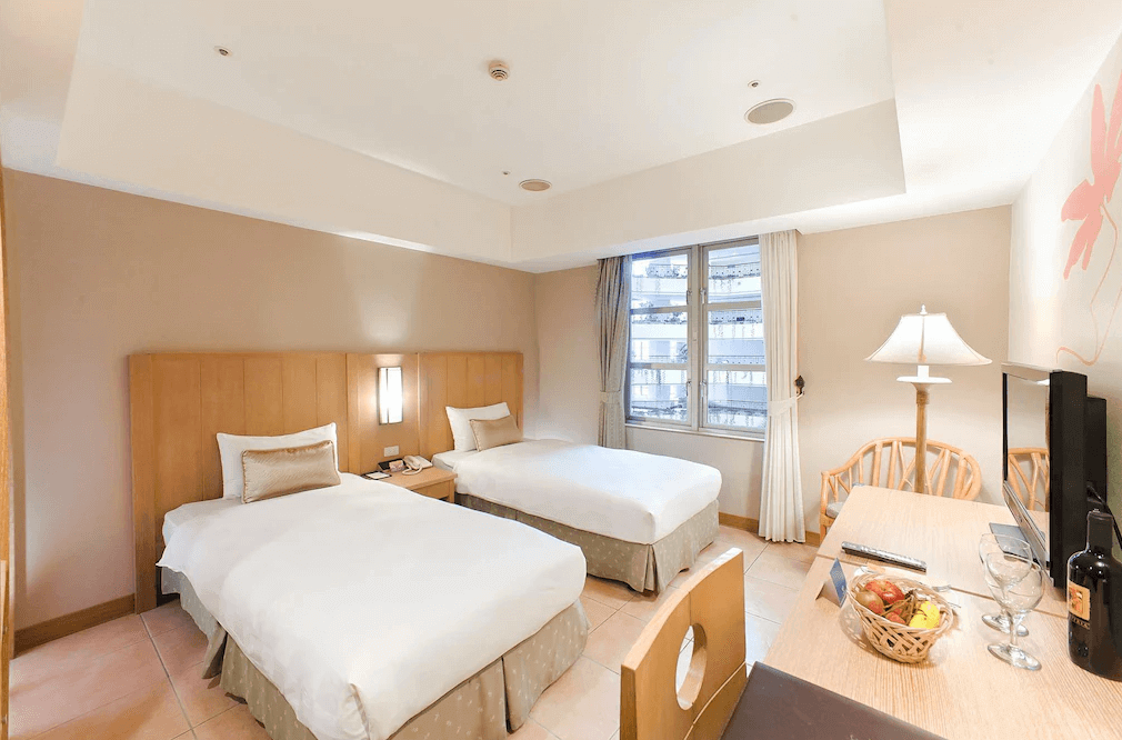 【古坑住宿】劍湖山渡假大飯店的雙床房，房間布置簡約溫馨，配有兩張單人床、書桌、液晶電視及水果籃，窗外可見市景，適合親子或朋友共住。