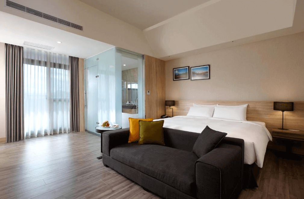 【新竹東區住宿】和選旅 THE HO HOTEL 現代簡約風格客房，配有大床、深灰色沙發與玻璃隔間浴室，整體空間明亮寬敞、木質調溫馨舒適。