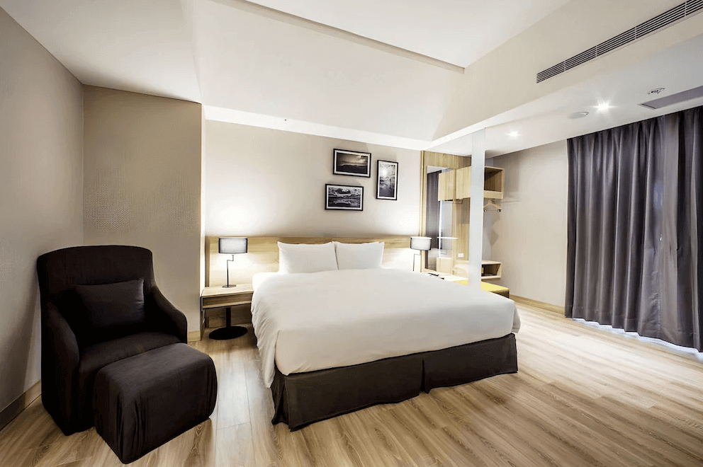 【新竹東區住宿】和選旅 THE HO HOTEL 溫馨大床房，設有休閒單椅與落地窗，木地板與簡約風格打造舒適放鬆的住宿氛圍。