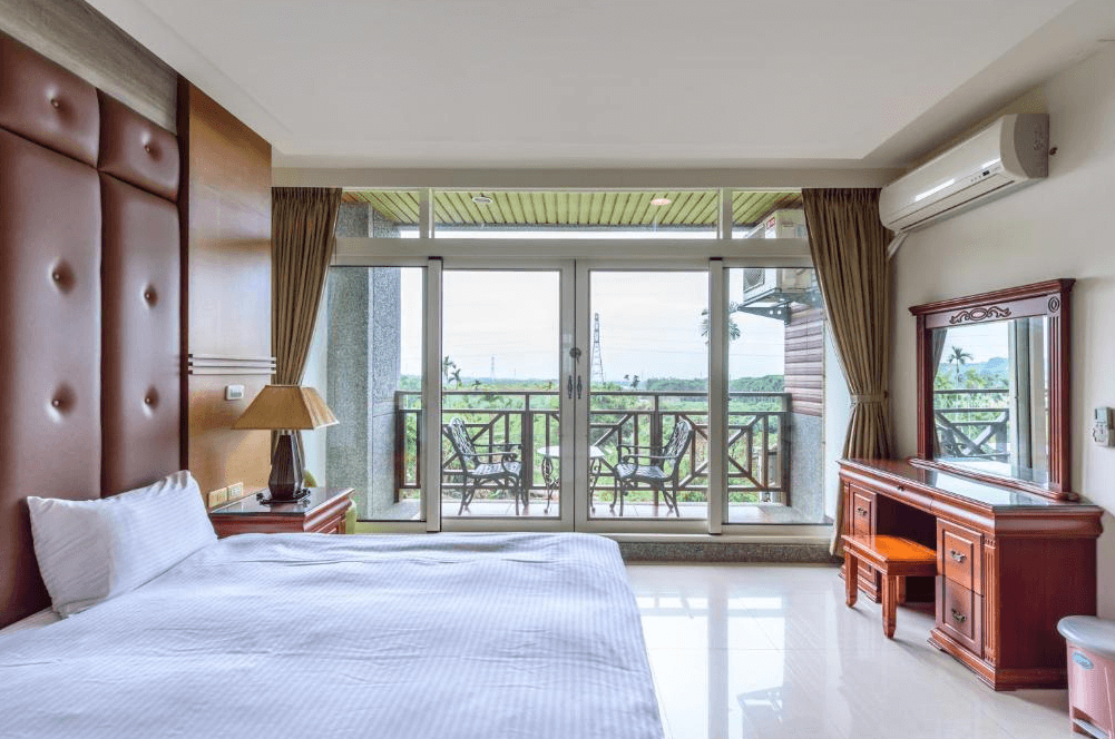 【古坑住宿】大湖山莊的景觀雙人房，設有一張雙人床、典雅木製梳妝台與陽台座椅，大片落地窗外可眺望田園綠意，室內空間明亮寬敞。