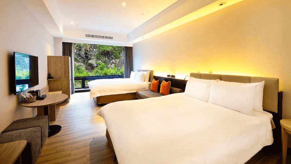 【花蓮寵物友善飯店】太魯閣晶英酒店的現代雙大床客房，設有大片落地窗可欣賞峽谷綠景，房內以暖色燈光與木質地板營造溫馨氛圍，附設沙發區與電視，適合家庭入住。