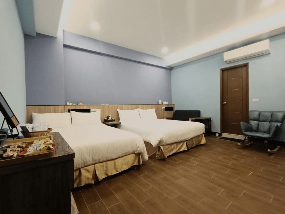 【竹山住宿】怡然自得民宿四人房，設有兩張雙人床，整體採木質地板與淺藍牆面設計，搭配搖椅與休息椅，空間寬敞明亮，營造舒適靜謐的住宿環境。