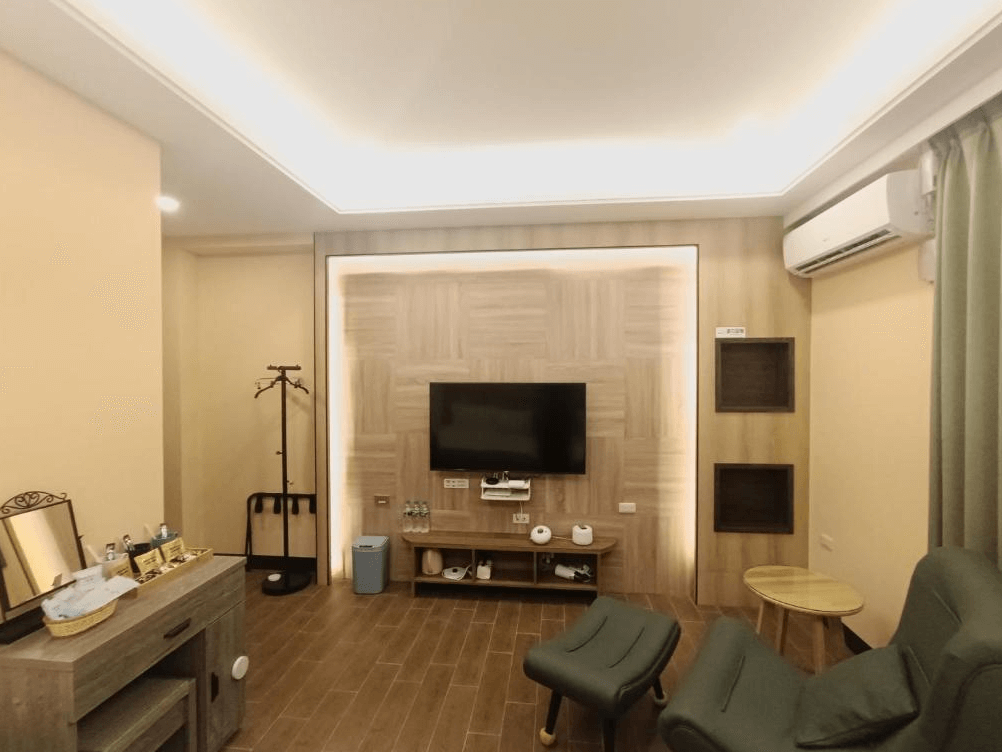 【竹山住宿】怡然自得民宿客房休憩空間，設有電視牆、綠色休閒椅與梳妝台，整體色調自然柔和，提供旅人自在舒適的休息角落。