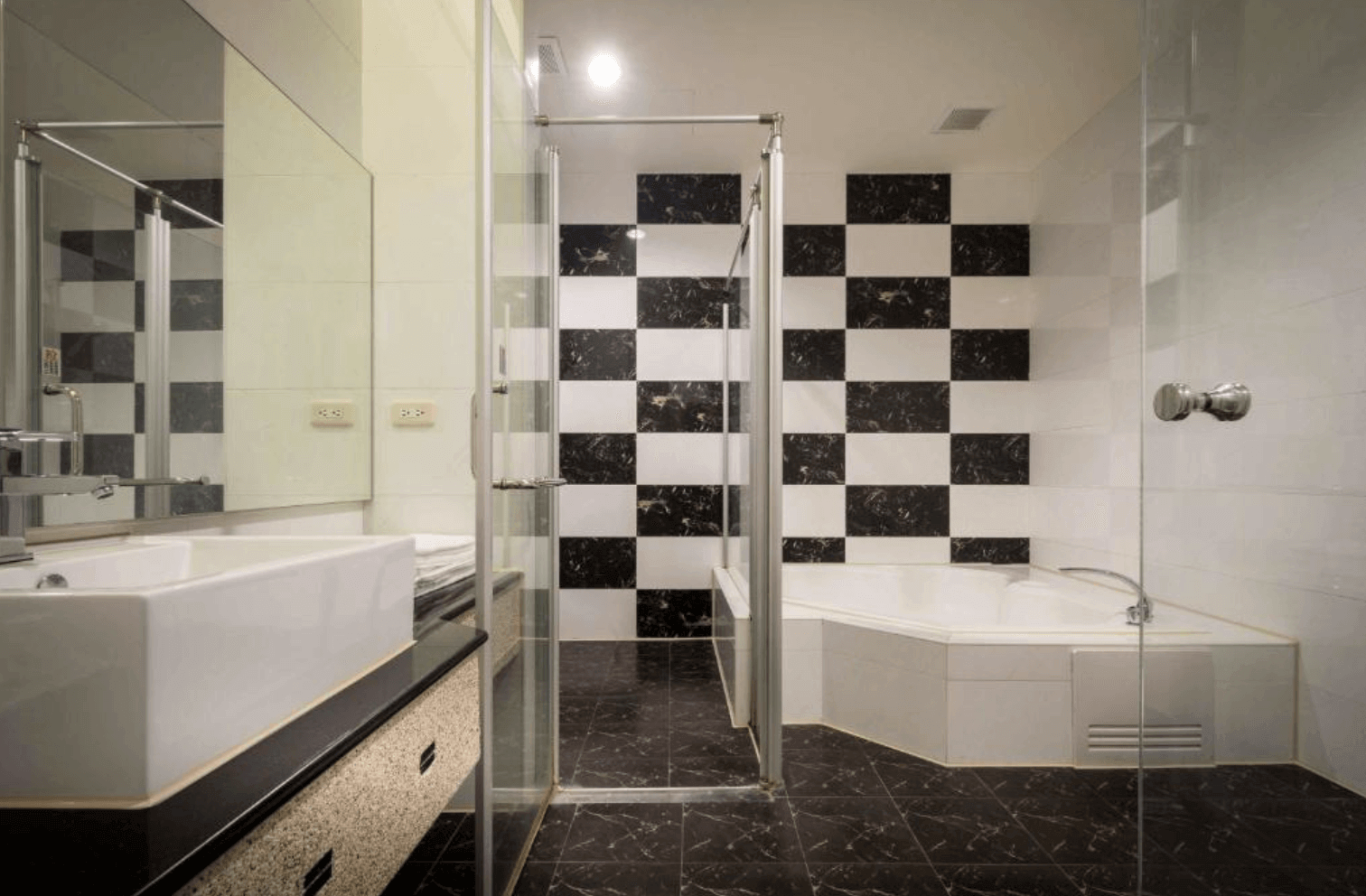 【清水住宿】愛力根汽車旅館黑白棋盤格設計浴室，設有角落浴缸與玻璃淋浴間，搭配大片鏡面與高質感洗手台，風格獨具。