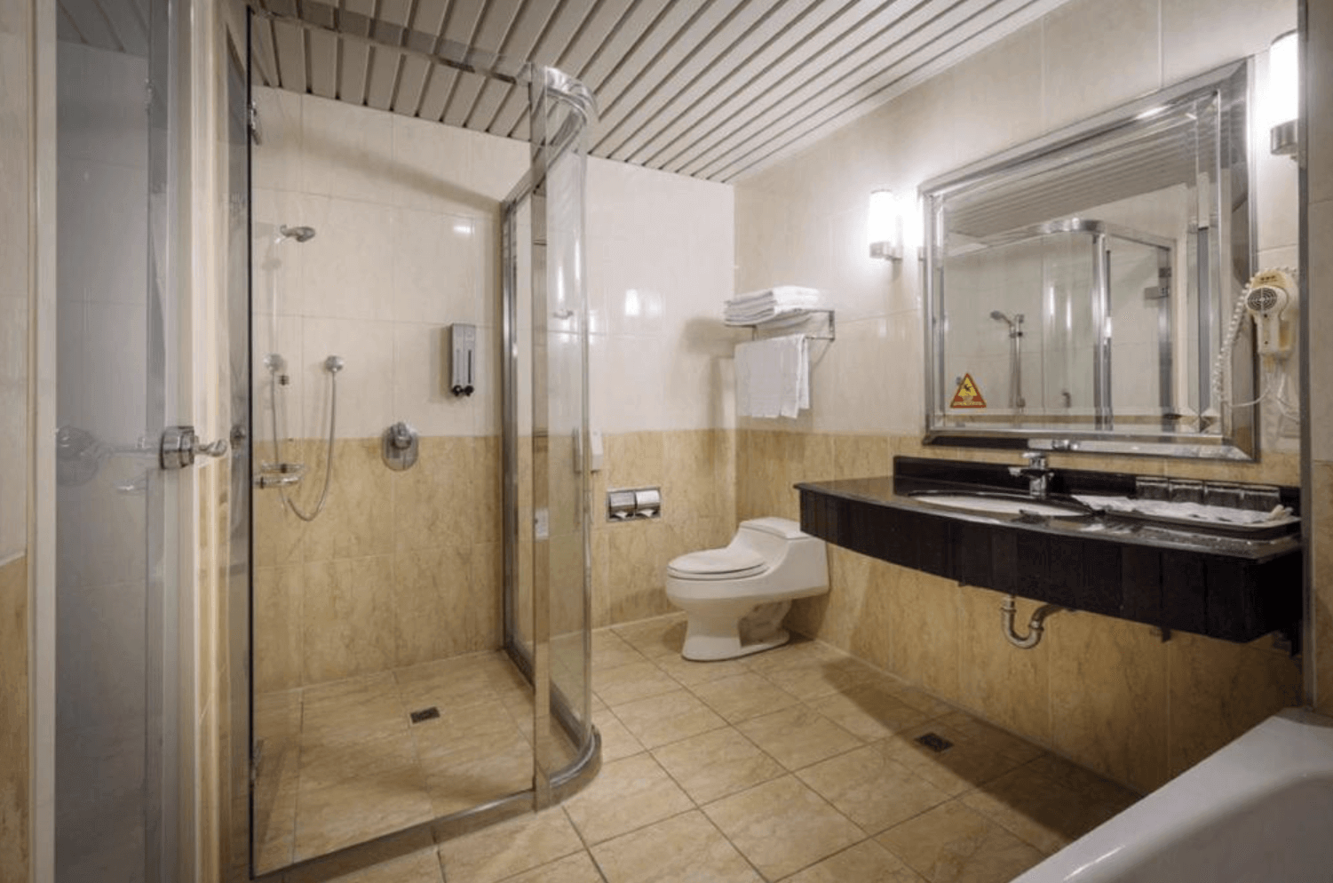 【中壢夜市住宿】承攜行旅－中壢中正館浴室設施一景，設有乾濕分離淋浴間、馬桶與雙人洗手台，採用米黃色磁磚，簡潔實用。