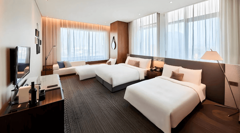 【新竹東區住宿】新竹伊普索飯店雙大床客房，搭配落地窗與簡約木質裝潢，另設有躺椅與多樣照明設備，適合家庭或多人入住。