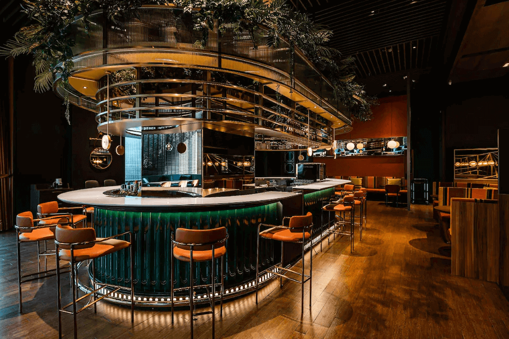 【新竹東區住宿】新竹伊普索飯店酒吧空間設計時尚，中央環狀吧台搭配橘色高腳椅與綠色燈光，營造夜間潮流社交氛圍。