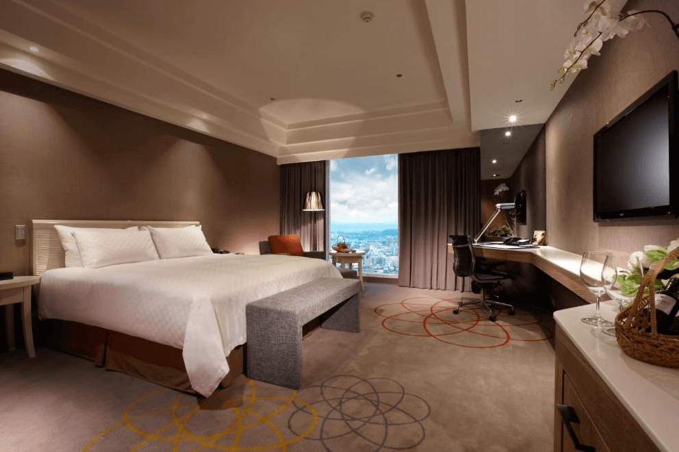 【新竹東區住宿】新竹老爺酒店精緻客房設計，擁有大片落地窗與城市景色，室內配置沙發、辦公桌與壁掛電視，風格典雅大方。