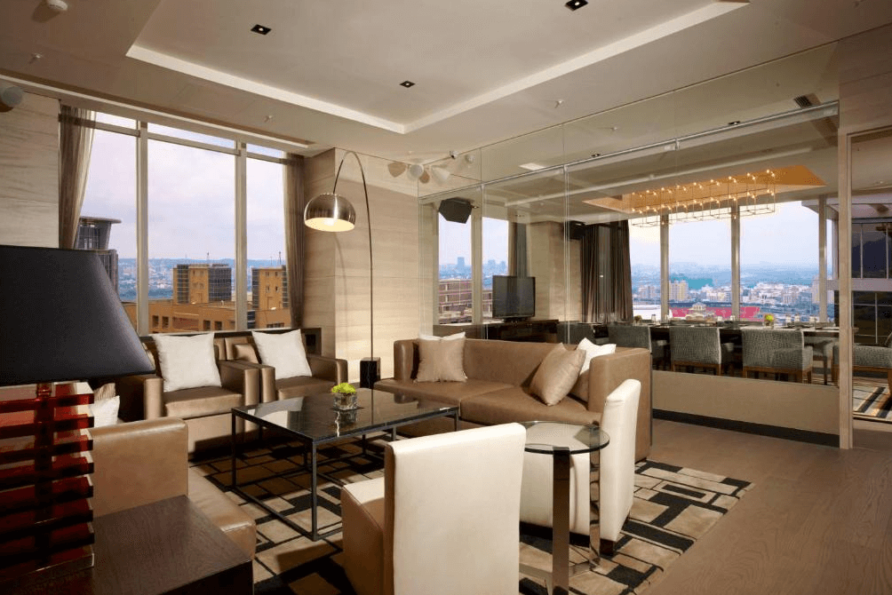 【竹北住宿】新竹豐邑喜來登大飯店高樓層行政套房客廳，大片落地窗俯瞰城市景觀，配有沙發、茶几與現代感燈飾，適合家庭或商務聚會。