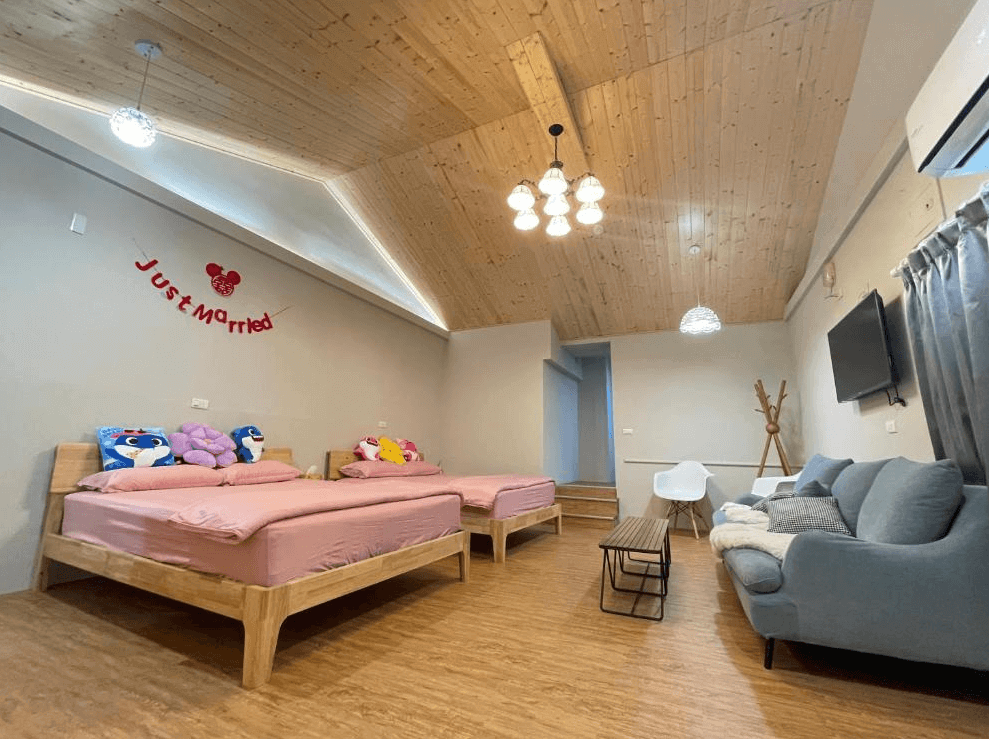 【西螺住宿】旅人路過時四人房，挑高木質斜屋頂搭配現代吊燈，空間明亮舒適，設有雙床、沙發、電視與小茶几，牆上掛有“Just Married”裝飾字樣。