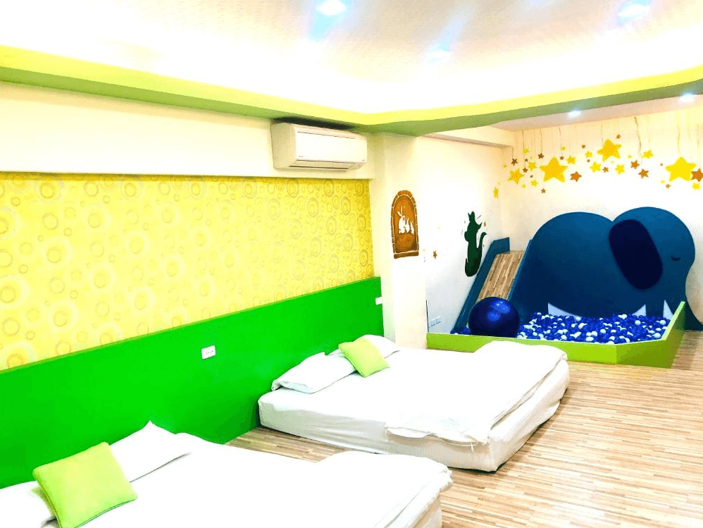 【竹山住宿】晚安熊親子民宿星星夜空主題房型，房內設有雙人床與象造型的球池滑梯遊戲區，搭配星星吊飾與綠黃牆面，充滿童趣與溫馨感。