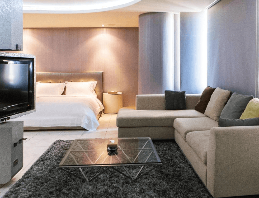 【竹山住宿】歐遊國際連鎖精品旅館竹山館現代簡約雙人套房，設有白色大床與米色L型沙發，搭配落地電視與玻璃茶几，整體風格柔和舒適，營造溫馨的住宿體驗。