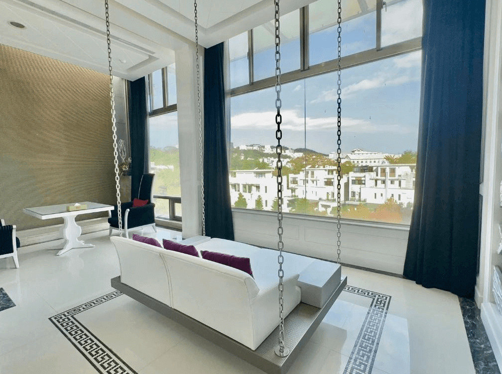 【新竹東區住宿】湖山風景旅館觀景沙發區，設有吊掛式白色沙發與大片落地窗，可俯瞰外部白色別墅群與山景，光線通透舒適。