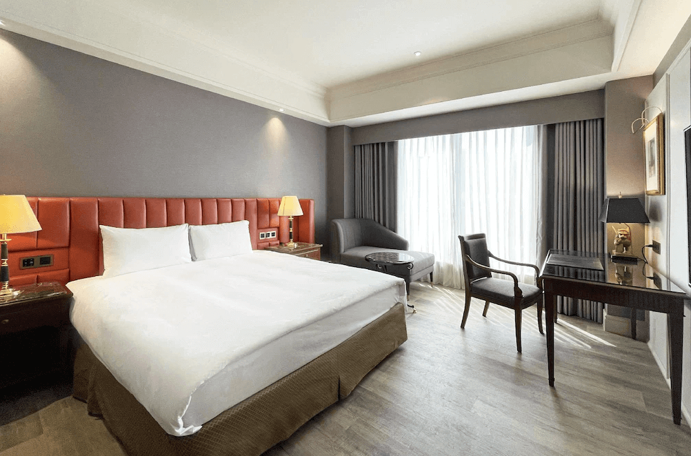 【新竹東區住宿】煙波大飯店-湖濱館大床房，柔和光線透過窗簾灑入室內，房內配有沙發、書桌與雙側床頭燈，空間寬敞溫馨。
