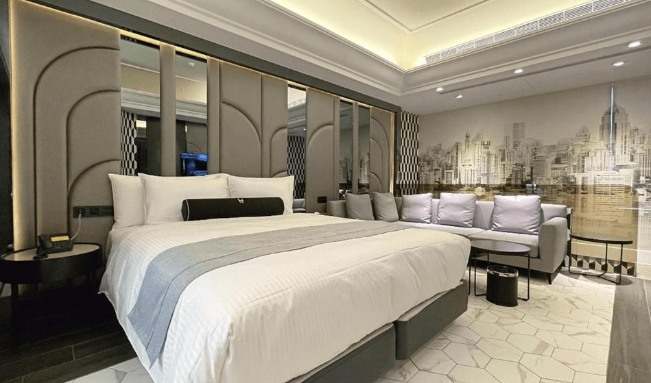 【竹北住宿】璽悅旅館現代設計風格雙人房，配有寬大雙人床與灰色沙發區，牆面為城市剪影壁畫，整體空間明亮高雅。