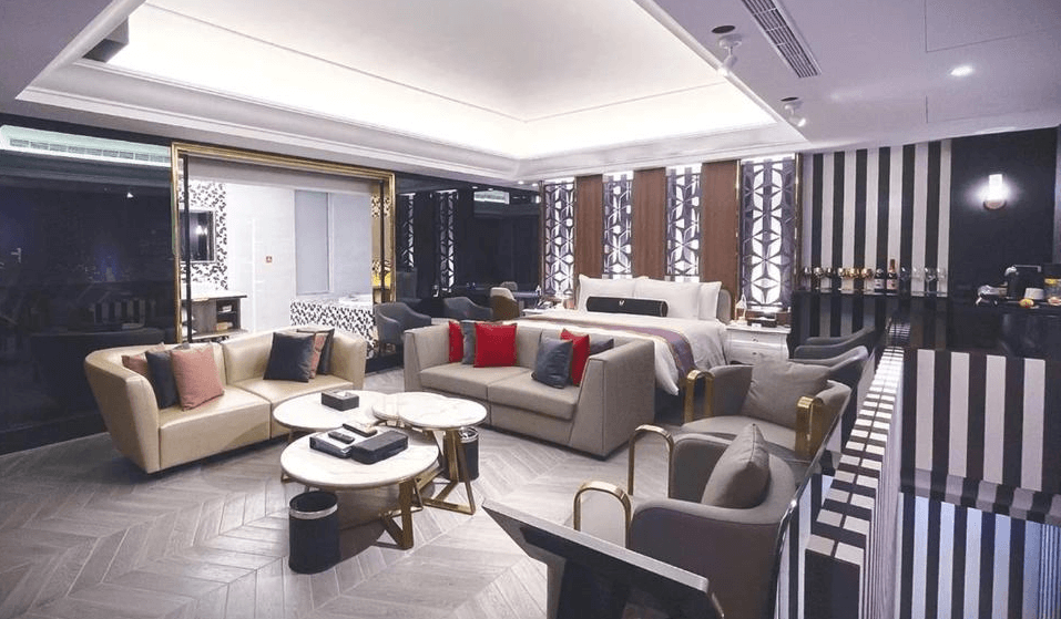 【竹北住宿】璽悅旅館奢華套房客廳空間，設有多組沙發與圓形茶几，房間後方為開放式雙人床與黑白條紋裝潢，展現摩登時尚感。