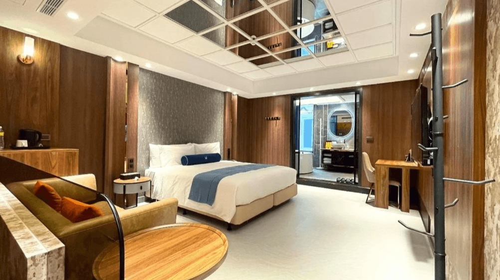 【竹北住宿】璽悅旅館溫馨木質風格客房，設有大型床鋪、柔和照明、沙發與書桌，浴室採透明玻璃隔間，兼具質感與功能性。