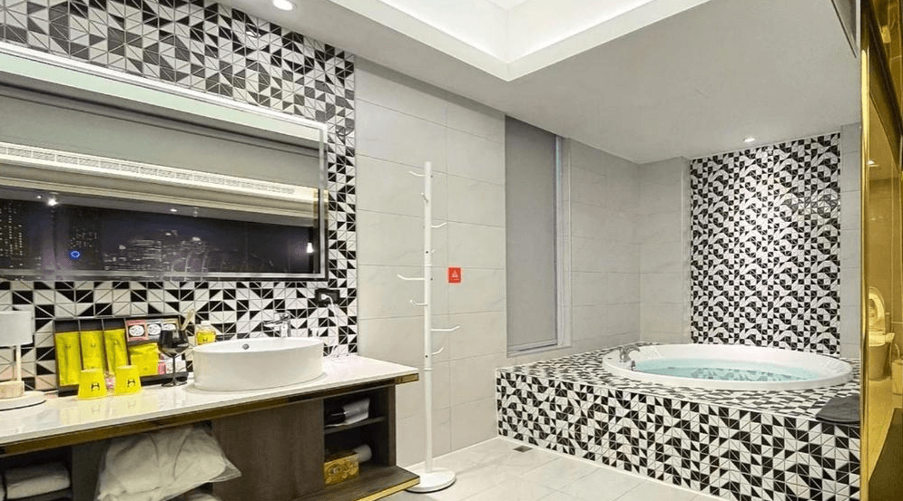 【竹北住宿】璽悅旅館現代化浴室設計，特色馬賽克磁磚牆面與圓形按摩浴缸，搭配白色檯面與圓鏡，營造出質感與放鬆兼具的空間。