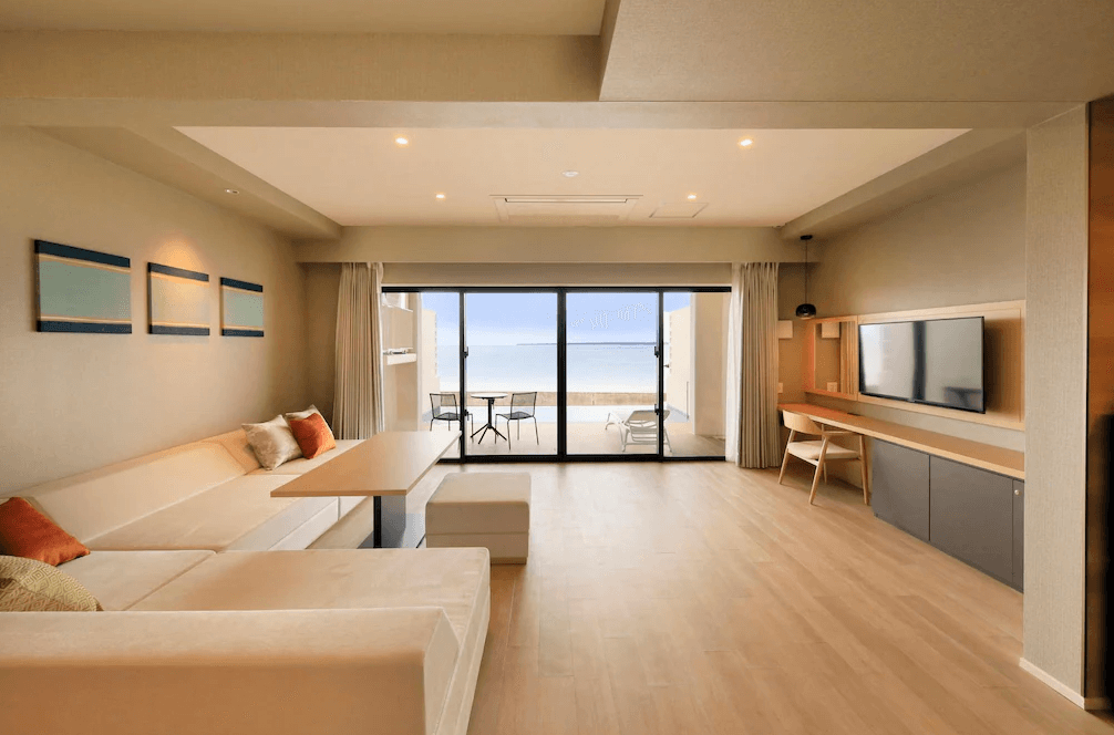 【石垣島住宿】現代感十足的石垣島VIVOVIVA客廳空間，設有L型沙發與餐桌，大片落地窗可遠眺蔚藍海景與私人陽台。