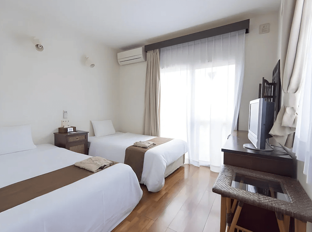 【石垣島住宿】石垣島帕提那酒店雙床客房，設有木地板與簡約傢俱，搭配棕白配色床組與柔和自然光，空間舒適整潔，適合輕旅行入住。