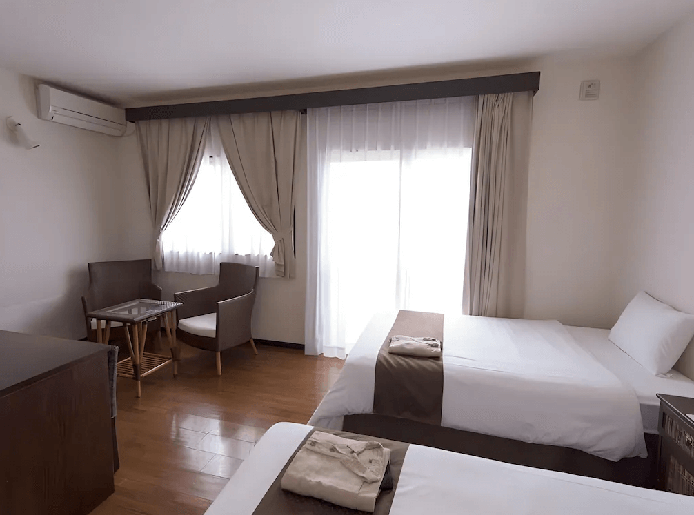【石垣島住宿】石垣島帕提那酒店雙人房內部空間，擺設兩張單人床與小餐桌椅組，窗簾拉開後可享受明亮採光，營造溫馨居家氛圍。