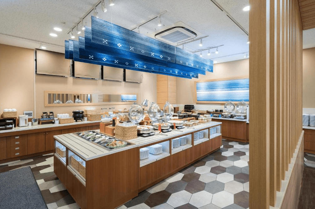 【石垣島住宿】石垣島船屋飯店早餐自助餐廳，提供多樣中西式餐點與飲品，設計以木質調與藍色海洋風吊飾營造出明亮舒適的用餐氛圍。