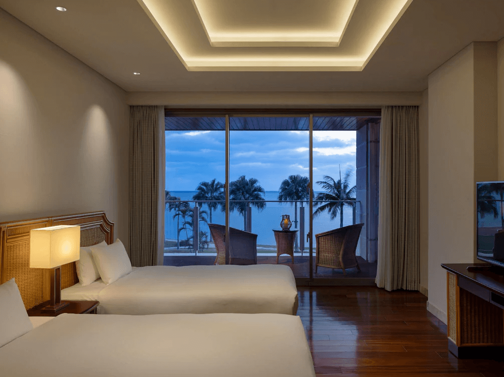 【石垣島住宿】石垣度假飯店夜晚海景房景色，兩張床面向陽台，窗外可見浪漫燈光與棕櫚樹海景。