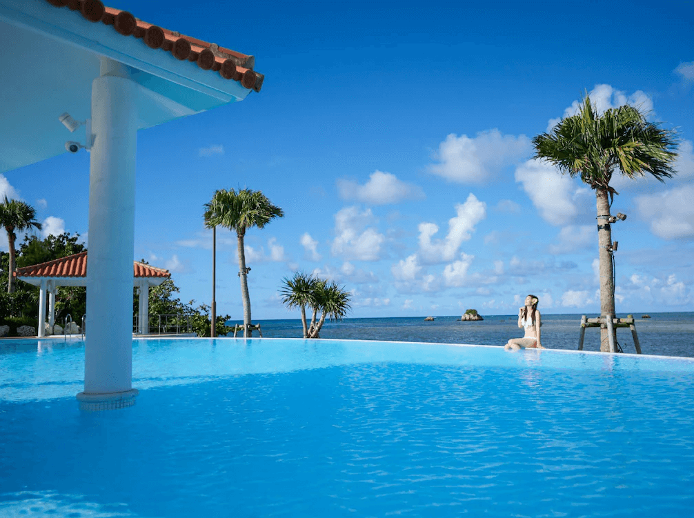 【石垣島住宿】石垣度假飯店無邊際泳池，旅客坐在泳池邊欣賞蔚藍海景與藍天白雲，熱帶風情十足。