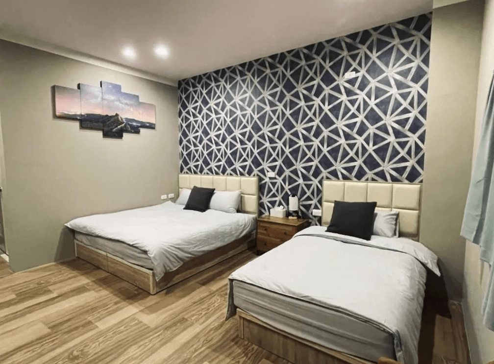 【竹山住宿】竹山。鄉間小路三人房房型，設有一張雙人床與一張單人床，牆面以深藍幾何花紋裝飾，木質地板與柔和燈光營造溫馨舒適的氛圍。