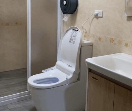 【西螺住宿】粨倉文旅浴室設施，內有白色馬桶、洗手台與獨立淋浴間，整體乾淨明亮，牆面為淺色花紋磁磚，簡約實用。