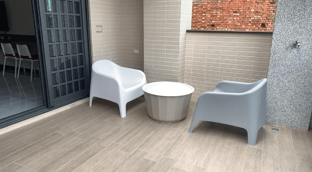 【西螺住宿】粨倉文旅陽台空間，擺放兩張簡約塑料休閒椅與小圓桌，地面為木紋磁磚設計，提供旅客放鬆聊天的休憩環境。