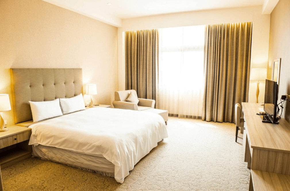 【古坑住宿】翠華會館的雙人房型，房內設有一張加大雙人床、舒適單人沙發與柔和燈光，空間寬敞明亮，整體風格溫馨典雅，適合情侶或商務旅客入住。