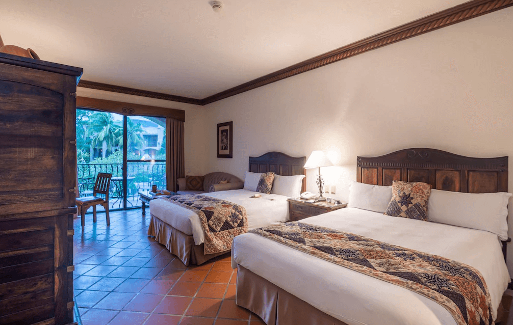 【花蓮寵物友善飯店】花蓮理想大地渡假飯店的客房內部，配有兩張雙人床、溫馨木質家具與復古風格的地磚，窗外可見棕櫚樹與陽台景觀，展現濃厚南歐度假氛圍。