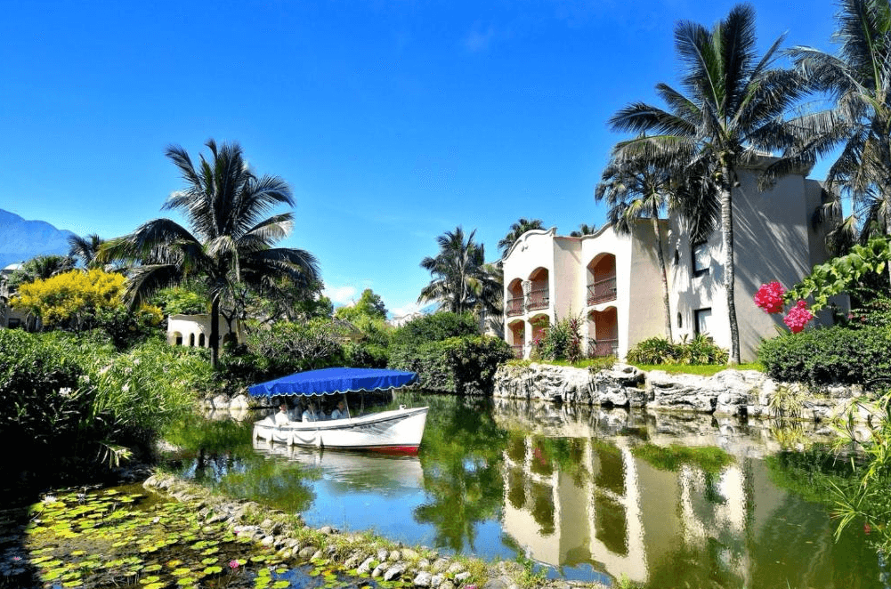 【花蓮寵物友善飯店】花蓮理想大地渡假飯店園區內的運河景觀與遊船，湖水倒映著棕櫚樹與西班牙式建築，環境綠意盎然，風景如畫。
