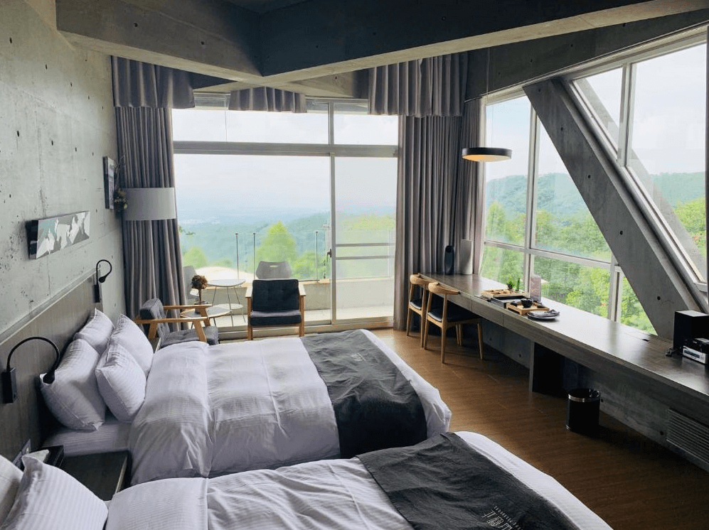 【古坑住宿】"古坑住宿精選示意圖"華山觀止-虫二行館的景觀雙床房，大片落地窗將遠山與綠意盡收眼底，搭配混凝土清水模設計風格，空間簡約時尚，擁有寬敞書桌與戶外陽台。