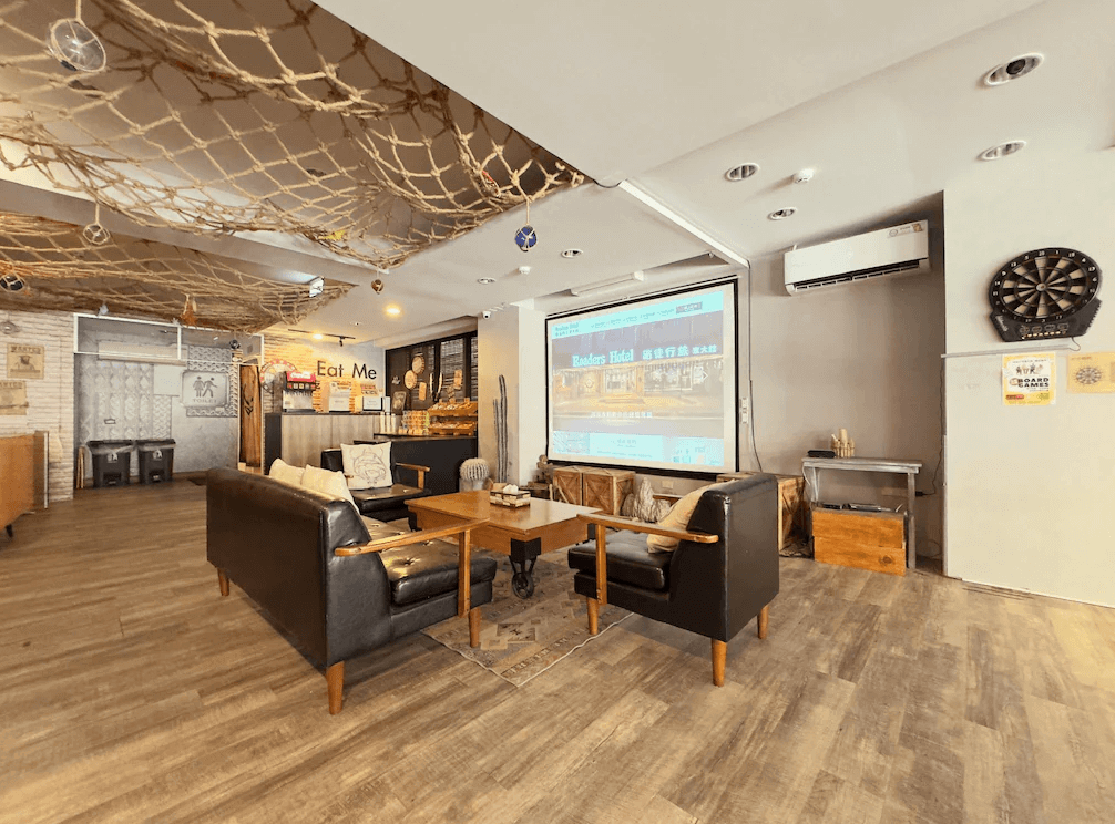 【花蓮寵物友善飯店】路徒行旅 花蓮東大館大廳交誼空間，設有舒適沙發區、投影幕與飛鏢機，天花板以繩網與海洋元素裝飾，營造濃厚冒險風格。