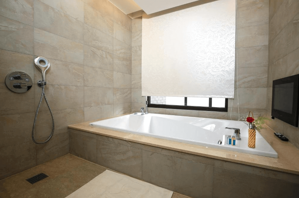 【新竹東區住宿】達龍商旅浴室空間，配備大浴缸與獨立淋浴設施，牆面與地板為米色系石材，設計高雅大器，旁設電視與擺飾花瓶。
