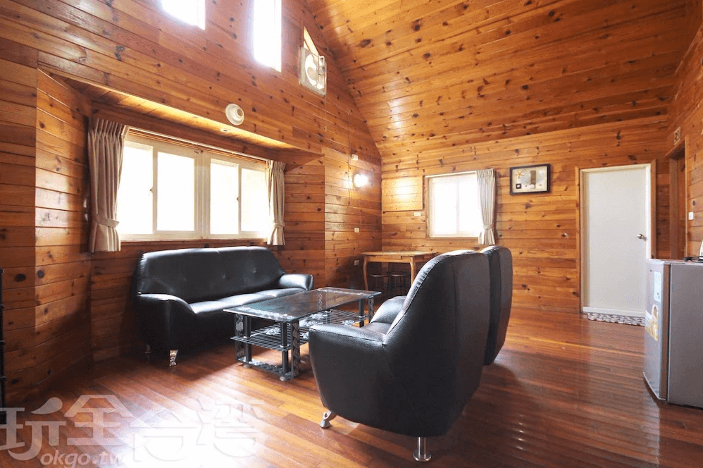 【竹山住宿】雙湖渡假山莊木屋室內公共空間，黑色沙發與木製餐桌組配置齊全，挑高窗戶採光良好，適合多人聚會或家庭休憩。