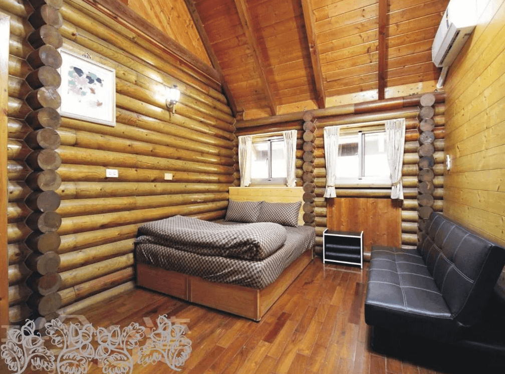 【竹山住宿】雙湖渡假山莊原木小屋雙人房型，特色圓木牆面設計展現濃厚山林風情，房內設有雙人床與黑色沙發床，適合情侶或家庭入住。