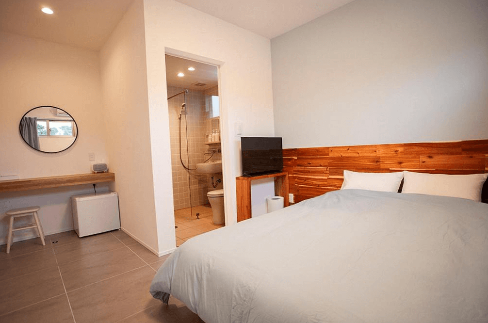 【名護住宿】Hichu House 雙人房，房內設有大床、梳妝桌與小冰箱，附帶衛浴設備，整體裝潢簡潔明亮，適合情侶或雙人入住。