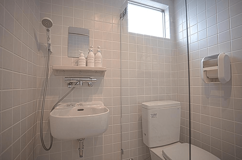 【名護住宿】Hichu House 浴室空間，採用淺色磁磚設計，內有洗手台、馬桶與淋浴設施，並提供洗髮乳與沐浴乳，乾淨明亮。