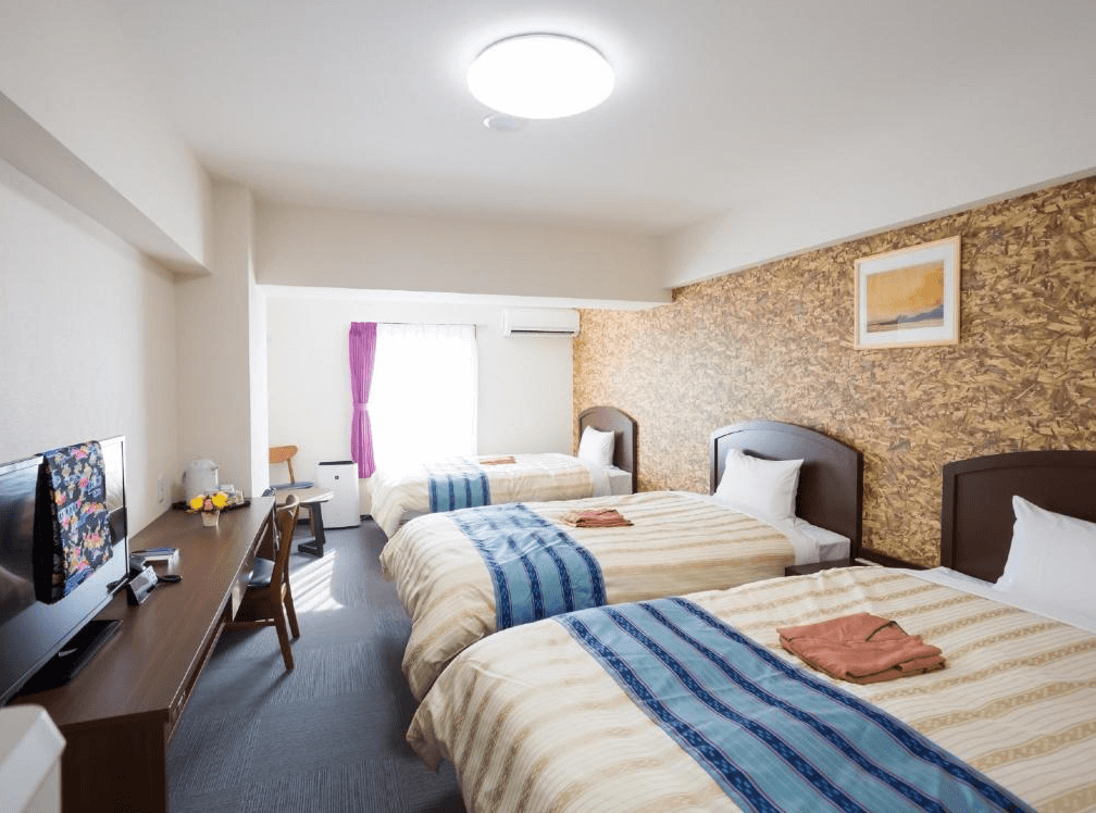 【名護住宿】Hotel Peace Island Nago 三人房，設有三張單人床，木質書桌搭配電視與簡約裝飾，房間明亮舒適。