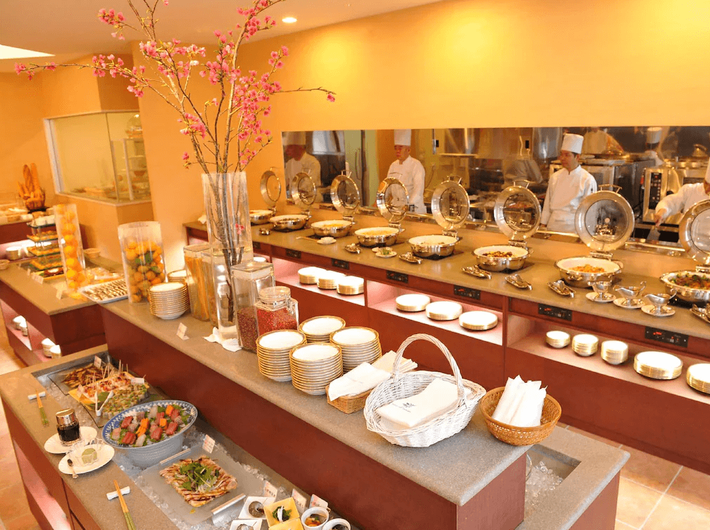 Yugaf Inn飯店沖繩 (Hotel Yugaf Inn Okinawa) 自助餐廳，多樣化餐點擺放整齊，前方有沙拉、冷盤與水果區，後方由廚師現場料理熱食，環境明亮溫馨。