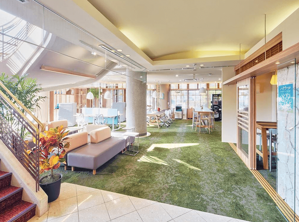 【名護住宿】Yugaf Inn飯店沖繩 (Hotel Yugaf Inn Okinawa) 大廳休憩區，綠色地毯搭配舒適沙發與桌椅，空間寬敞明亮，適合旅客交流與放鬆。