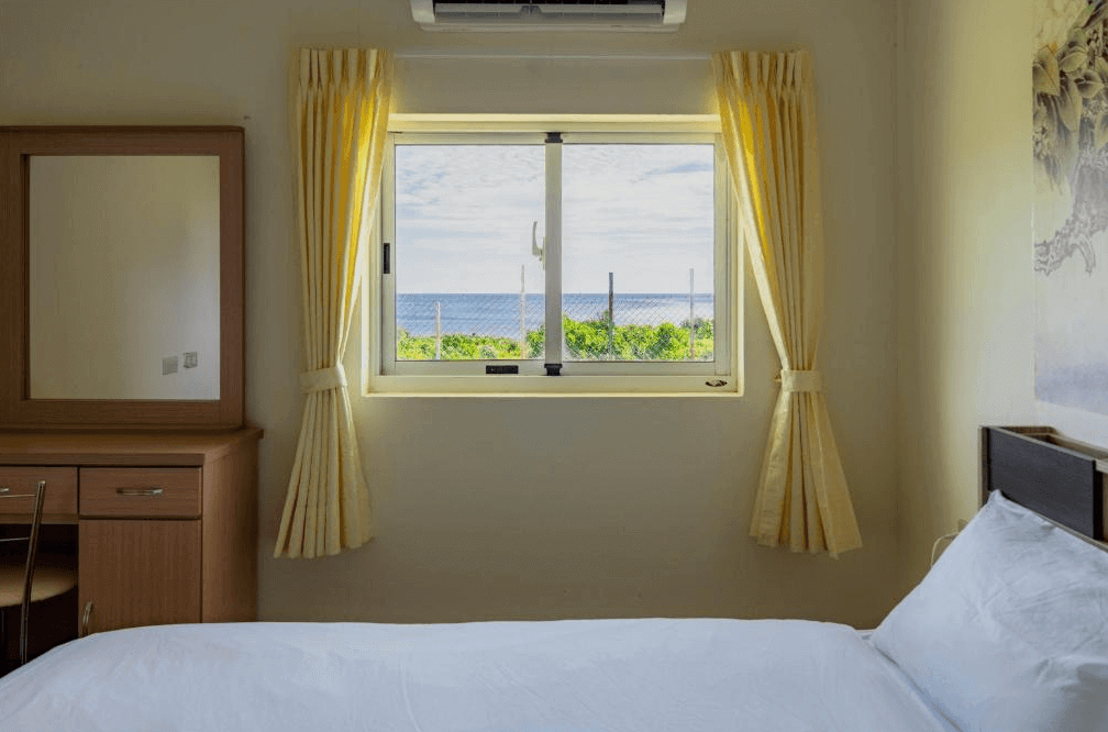 【蘭嶼住宿】伊那部海景民宿海景房：房間窗外即可看到藍色大海，搭配黃色窗簾與木質梳妝台，簡潔舒適。