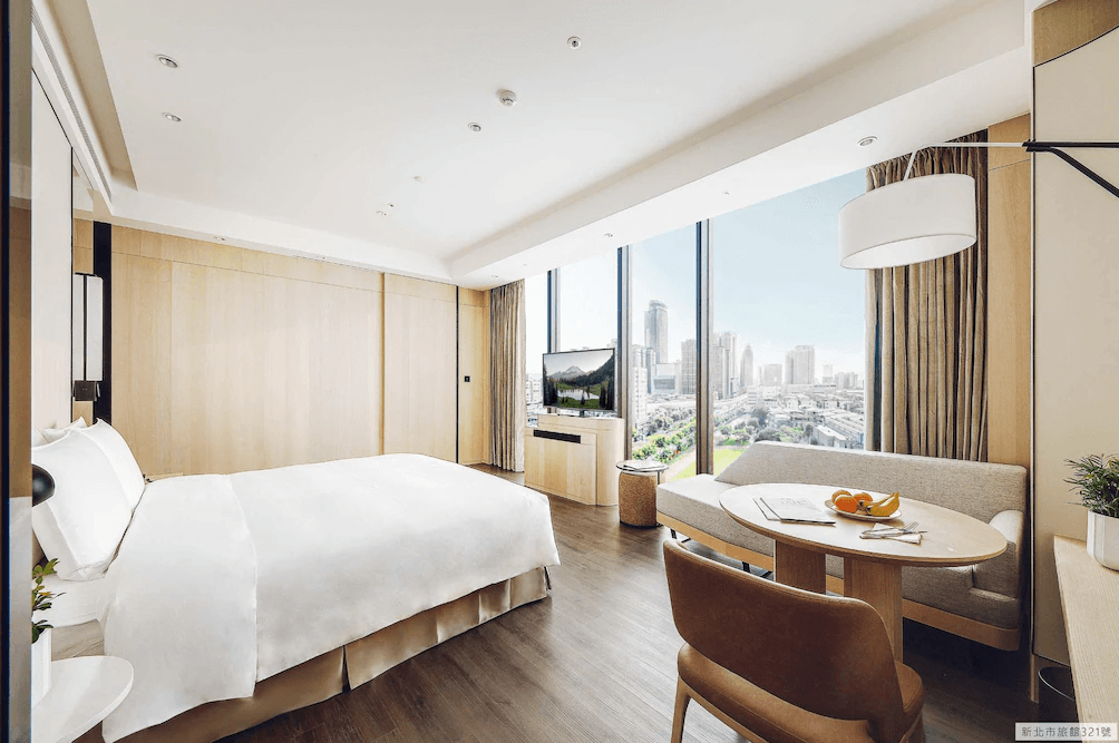 【板橋住宿】傑仕堡有氧酒店 高樓層景觀房，大床搭配落地窗，可俯瞰都市風景，房內設有沙發與圓桌，營造溫馨住宿氛圍。