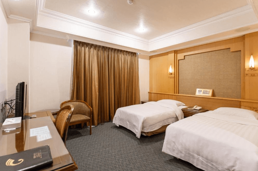 【板橋住宿】冠君大飯店 雙床房，採用木質裝潢與暖色燈光設計，設有書桌、電視與窗邊座椅，空間寬敞舒適。