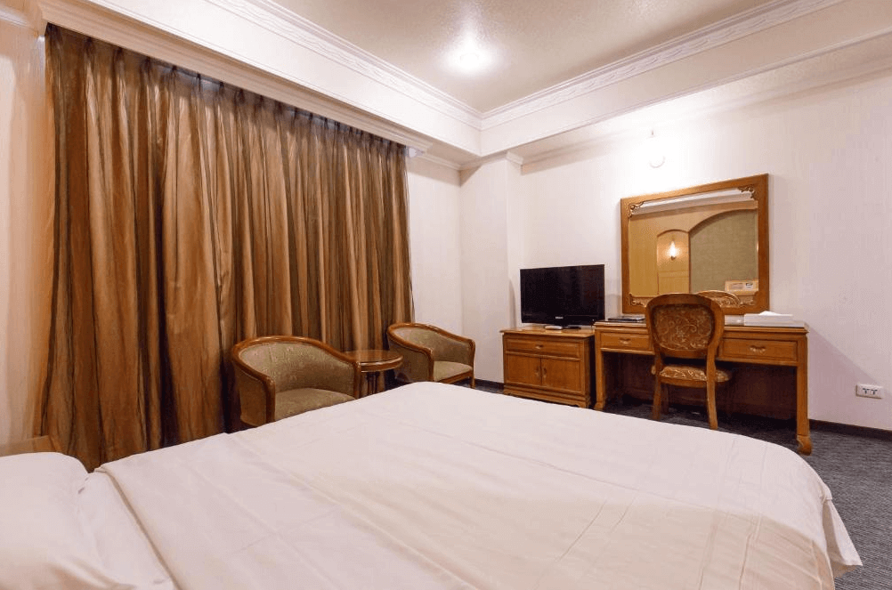 【板橋住宿】冠君大飯店 客房內景，設有大床、書桌與電視，窗簾拉起後可見自然光，整體設計簡潔典雅。